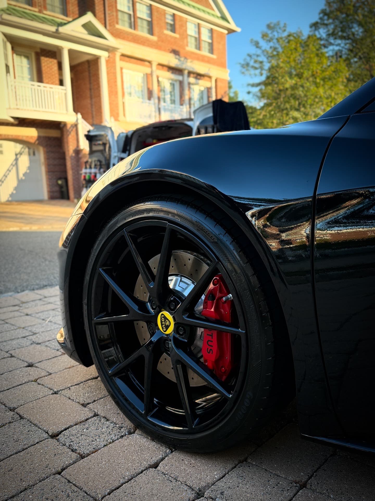Glossy black sports car wheel with a red brake caliper at golden hour
