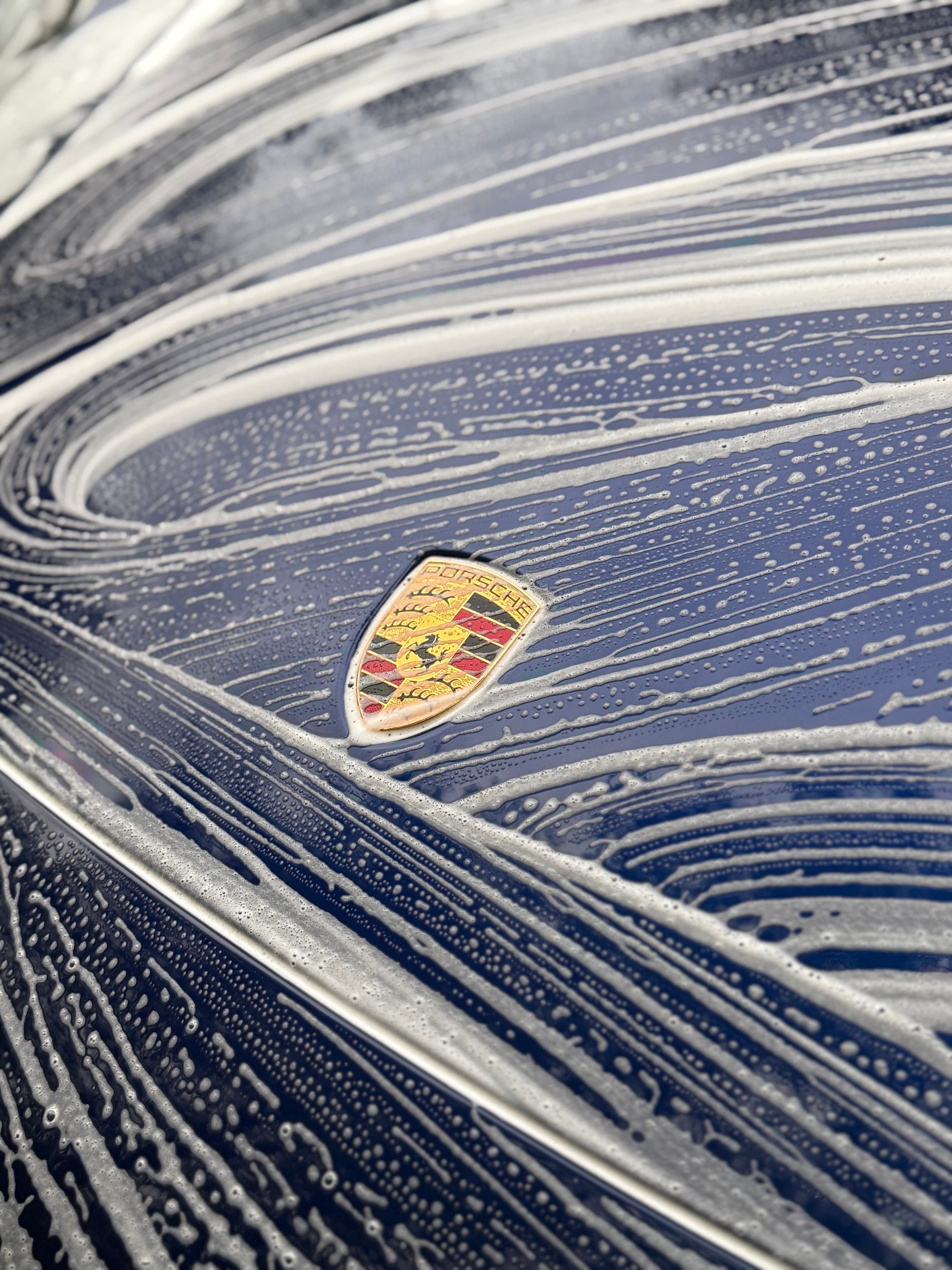 Foam wash swirling over the Porsche crest on a deep blue hood