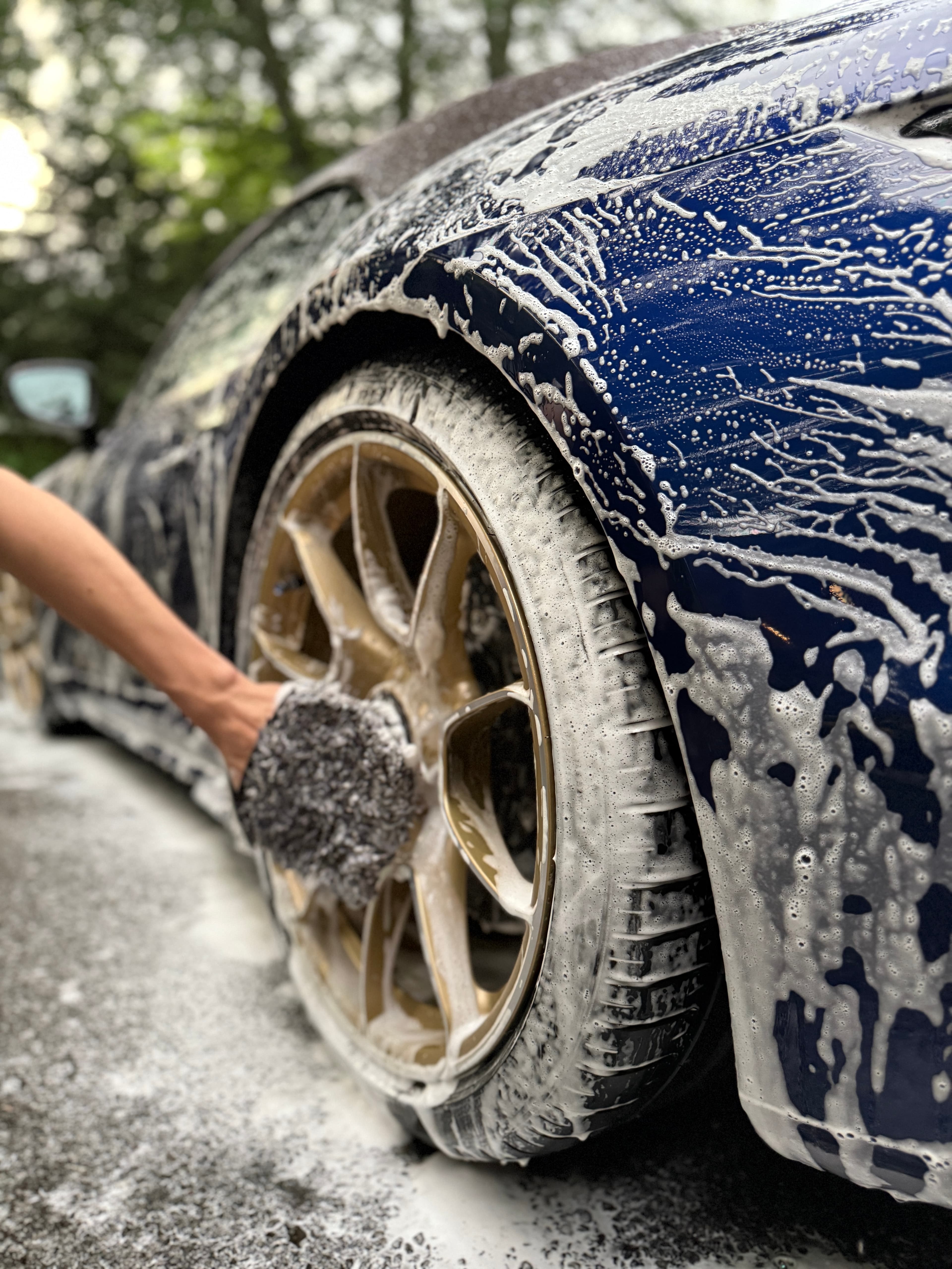 Hand-washing a foam-covered wheel with a wash mitt on a mobile detail
