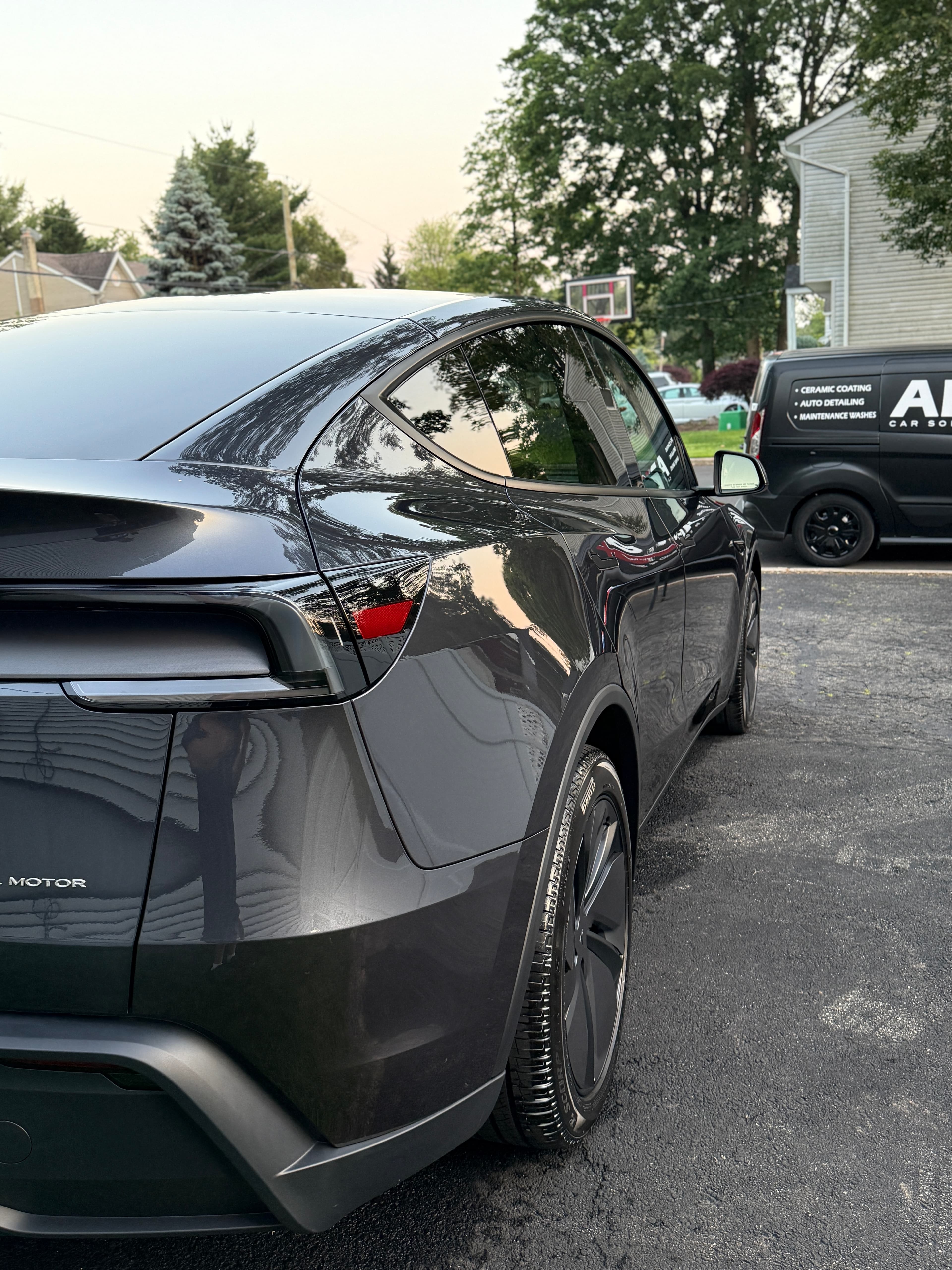 Freshly detailed gray Tesla Model Y with the APX mobile detailing van parked in a Hackensack office lot