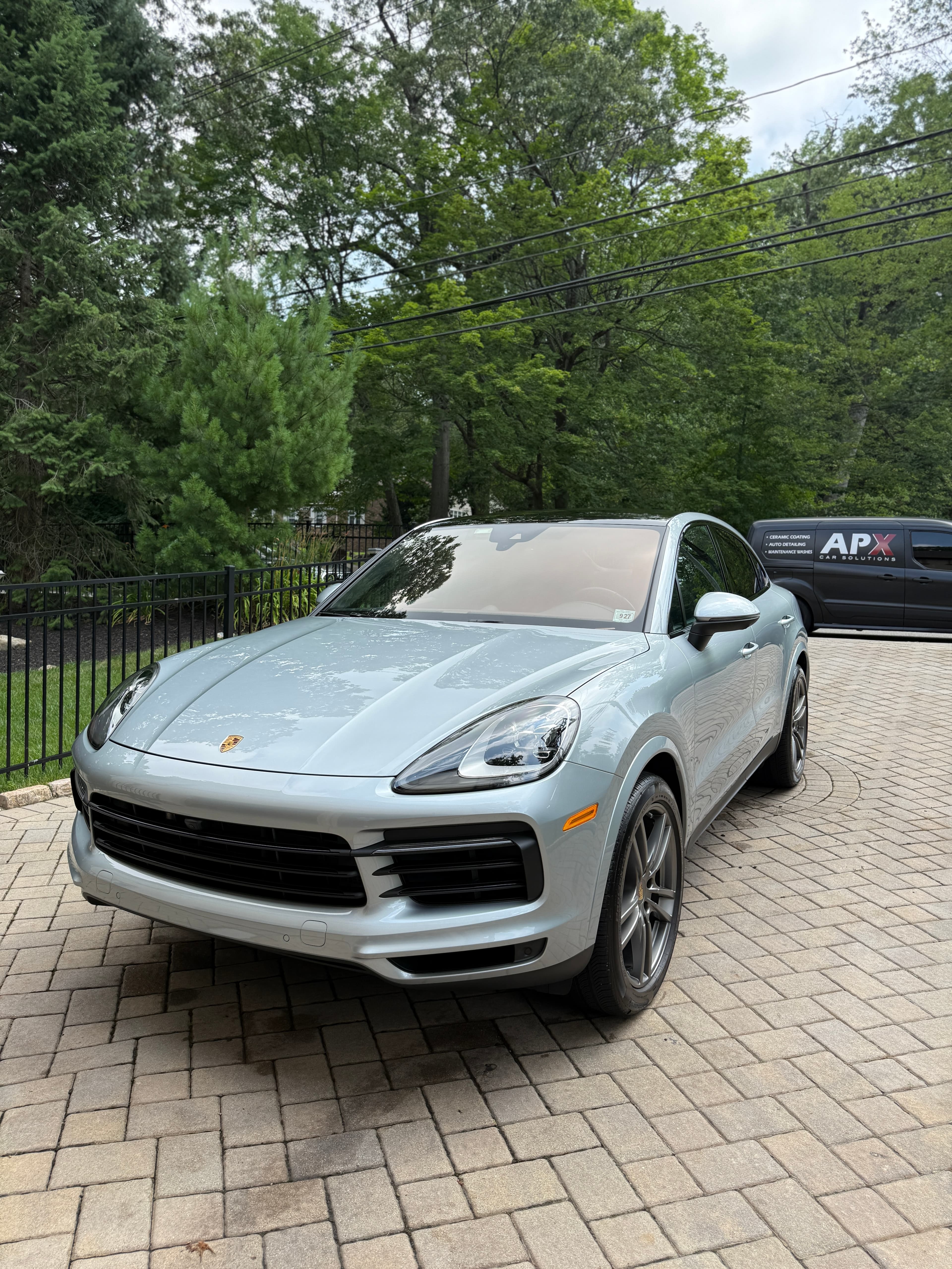 Silver Porsche Cayenne freshly detailed in a Waldwick driveway with the APX van behind it